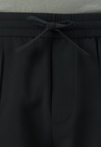 Schwarze Shorts mit elastischem Bund und vorderem Bindedetail, verfügt über eine glatte Textur und einen subtilen Glanz, entworfen für Komfort und Stil.
