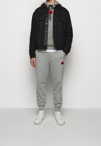 Chaqueta de mezclilla negra, sudadera gris con parche rojo, pantalones de chándal gris claro y zapatillas blancas. Todos los artículos tienen un ajuste casual y holgado.