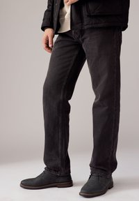 Čierne džínsové nohavice s priamym strihom, s mierne vyblednutou textúrou. Kombinované s tmavosivými členkovými topánkami a čiernou prešívanou bundou.