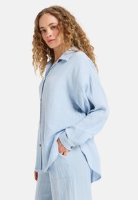 Lichtblauw, gestructureerd, overhemd met knoopsluiting, met kraag, lange mouwen en een ontspannen pasvorm. Heeft een zak en subtiele kreukels in de stof.