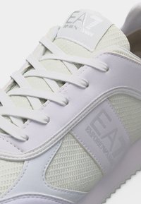 Λευκό αθλητικό παπούτσι EA7 Emporio Armani με υφασμάτινο δίχτυ, δερμάτινες επικαλύψεις, λογότυπο στη γλώσσα και κλείσιμο με κορδόνια.