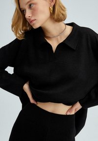 Črn oversized pulover s ovratnikom in podrobnim šivanjem; mehak material, široki rokavi in krojen dizajn.