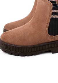 Botas de tobillo de ante marrón con paneles elásticos negros texturizados, suelas de goma y un diseño ligeramente elevado. Presenta rayas horizontales en los paneles.