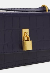 Borsa in pelle blu con stampa coccodrillo, caratterizzata da una chiusura a lucchetto dorato, una texture liscia e cuciture a contrasto lungo i bordi.