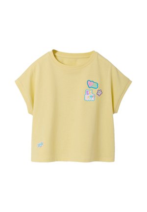 Light yellow short-sleeve crop top with colorful patches: a smiling heart, "BE HAPPY" text, small flower near the chest, and two blue flowers near hem.