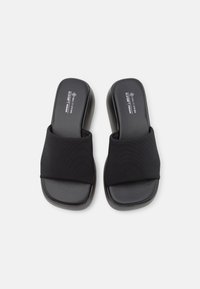 Par af sorte åbne slide-sandaler med brede stofremme og polstrede såler på en hvid baggrund.