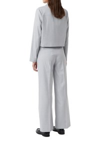 Lichtgrijze, cropped blazer met lange mouwen en textuur, gecombineerd met wijde broekspijpen, ook in lichtgrijs, en zwarte schoenen.