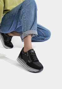 Baskets noires à finition texturée, dotées d'une fermeture éclair et de lacets, avec une semelle rayée. Matériaux comprenant du daim et des accents synthétiques.