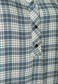Ein tailliertes Hemd im karierten Muster aus Blau, Schwarz und Weiß mit gelben Akzenten. Verfügt über schwarze Knöpfe und einen weichen, strukturierten Stoff.