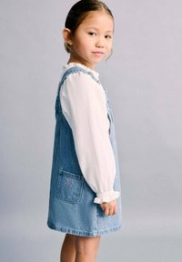 Džínové šaty na traky světle modré barvy s přední kapsou s motivem "Hello Kitty". Nosit přes bílou texturovanou blůzu s volánkovými rukávy.