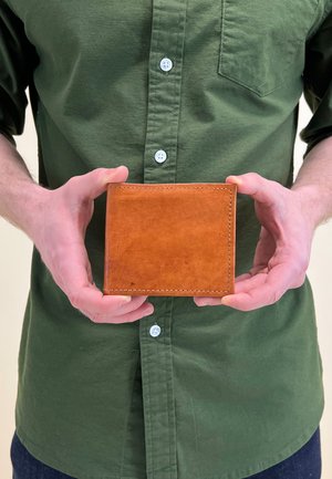 Braune Lederbörse mit sichtbaren Nähten, in Händen präsentiert, mit glatter Oberfläche und flacher rechteckiger Form.