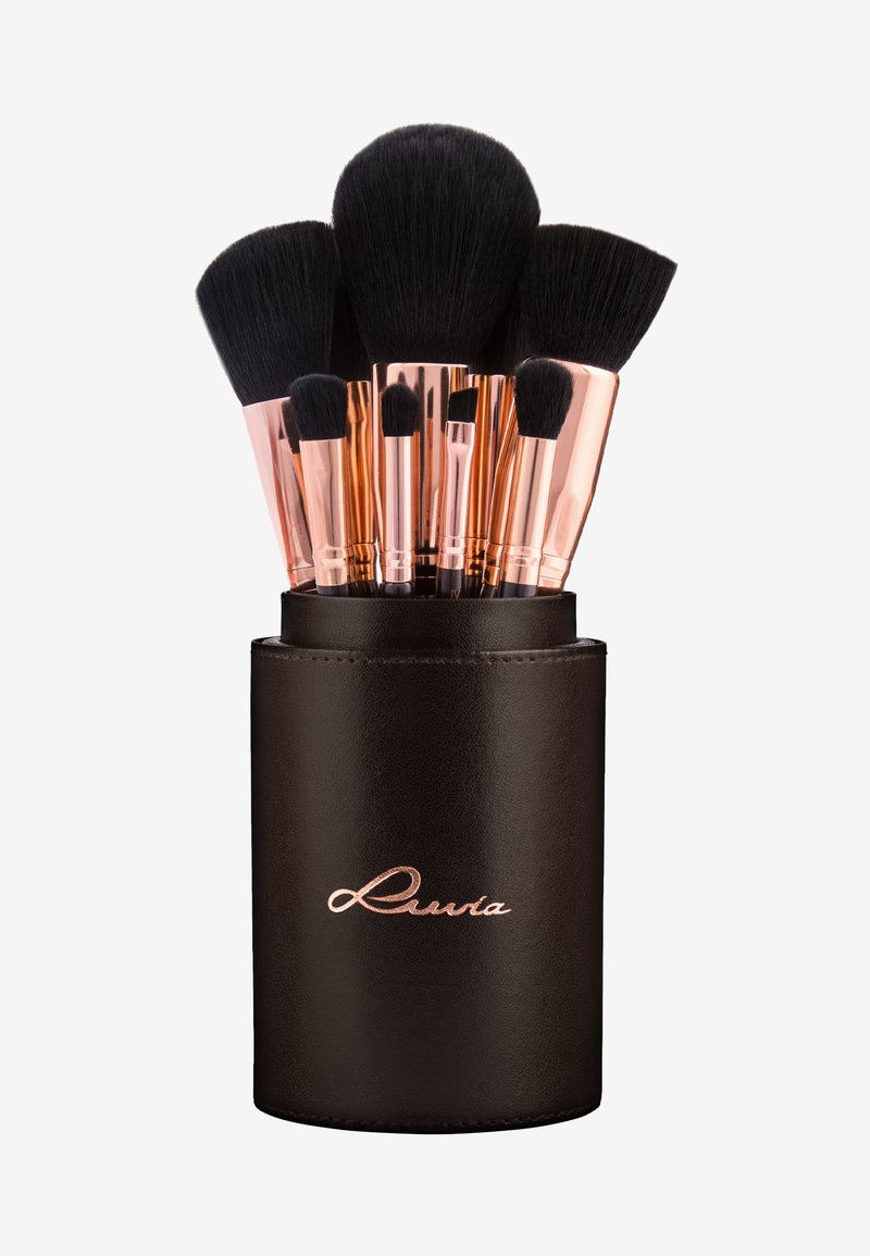 Set di pennelli per trucco con setole nere e ferrule in oro rosa, contenuti in un portapenne cilindrico in pelle marrone scuro con logo impresso.