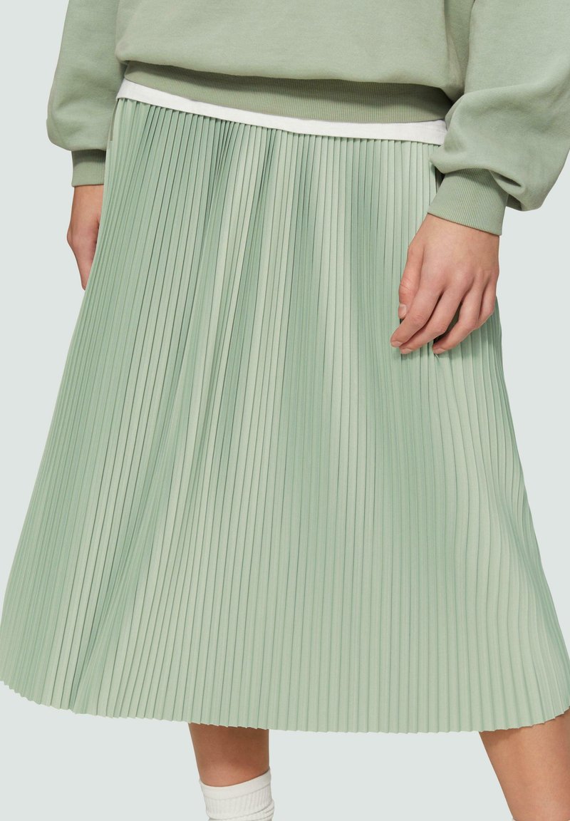 Lichtgroene geplooide rok met een witte tailleband. De stof is glad en heeft een textuur met verticale plooien, die tot halverwege de kuit reiken.