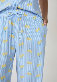 Set di pigiama a righe blu e bianche con vita regolabile, con un motivo di ciliegie gialle e gambi verdi su tutta la stoffa.