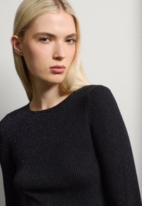 Zwarte geribbelde trui met een ronde hals, met subtiele glitters en een aansluitende textuur. De mouwen zijn aangesloten en soepel.