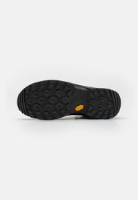 Sole di scarpa in gomma nera con un motivo di battistrada rugged, caratterizzata da un accento centrale in gomma gialla e elementi di trazione pronunciati in tutta la superficie.