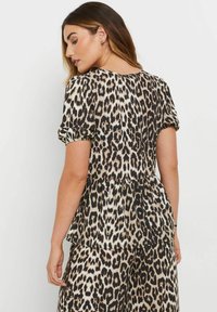 Top de estampado de leopardo en tejido ligero con mangas cortas abullonadas, dobladillo peplum y puños elásticos. Paleta de colores en negro y beige.