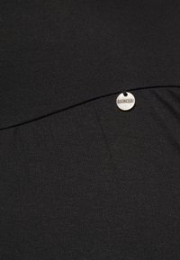 Top de tecido elástico preto com uma costura horizontal e uma etiqueta metálica circular com a inscrição "LOVE2WAIT" presa ao lado.