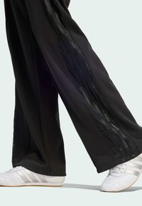 Black athletic pants with side mesh panels and stripes, paired with white shoes featuring silver accents and a textured design.