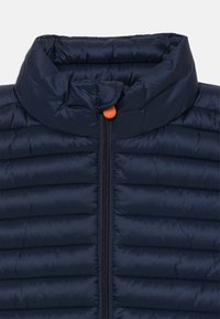 Námornícky modrá prešívaná péřová bunda s golierom, čiernym zipsom a malým oranžovým tlačidlom v hornej časti.