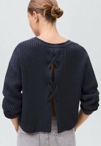 Pulover tricotat navy, cu o croială lejeră, textură striată și un spate deschis cu detalii de dantelare în cruce. Mâneci lungi, răsucite.