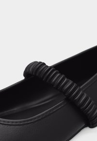 Μαύρο επίπεδο παπούτσι με στρογγυλεμένη μύτη και υφασμένη, ελαστική λουρίδα στο πάνω μέρος για ασφαλή εφαρμογή και στιλ.