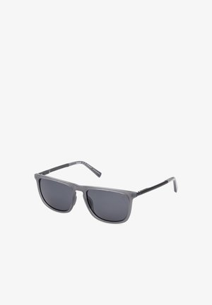 Rechteckige schwarze Sonnenbrille mit dunkel getönten Gläsern und schlanken, leicht gebogenen Bügeln auf weißem Hintergrund.