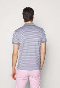 Kortärmad polo skjorta för män med navy- och vita ränder, stickat tyg, krage och kontrasterande fålldetaljer. Bärs med ljusrosa byxor.