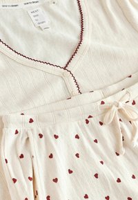 Lysekræm loungewear sæt med ribbet tekstur, maroon accenter og små røde hjerte mønstre. Inkluderer en knap-op top med V-hals.