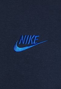 Mörkblått tyg med en texturerad yta som har en broderad Nike-logotyp i klarblå, som visar varumärkesnamnet och den ikoniska swoosh-designen.