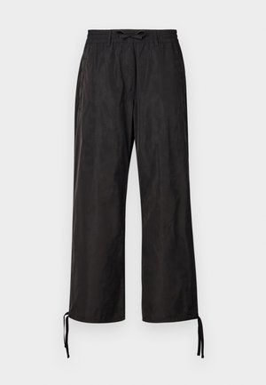 Zwarte, losvallende broek met een elastische tailleband en verstelbare koorden bij de enkels. Glad stof met een subtiele glans.