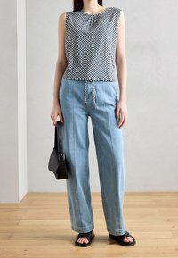 Modrý vzorovaný bezrukávový top s kulatým výstřihem, doplněný o světle modré kalhoty s širokými nohavicemi a páskem na stažení. Černá kabelka přes rameno a sandály.