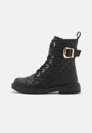 Black quilted leather ankle boot with laces, gold eyelets, a side buckle strap, and a pull tab at the back on a flat rubber sole.