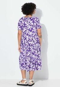 Lila Batik-Maxikleid mit kurzen Ärmeln, gestuftem Design und weichem Material. Es hat einen runden Ausschnitt und unterschiedliche lila Muster.