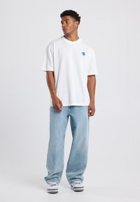 Camiseta de algodón blanca de manga corta con un diseño de flor azul, combinada con unos vaqueros de denim de corte holgado en un lavado claro y zapatillas blancas.