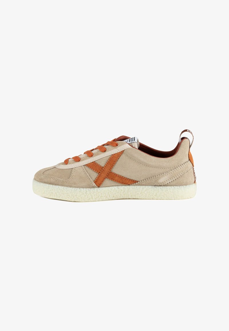Baskets en daim beige avec lacets orange et grand "X" orange brodé sur le côté, semelle blanche texturée et languette au talon.