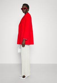 Rød oversized blazer, pink mønstrede sweater under, hvide teksturerede brede bukser, hvide hæle med neongrønne detaljer og hvid taske.