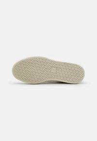 White sneaker outsole with a textured rubber surface, featuring a hexagonal pattern and embossed logo in the center for grip and support.