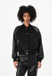 Čierna bunda s koženými rukávmi, rebrovanými manžetami a predným zapínaním na gombíky. Vyrobená z texturovanej látky, s elegantnými líniami a priliehavým strihom.