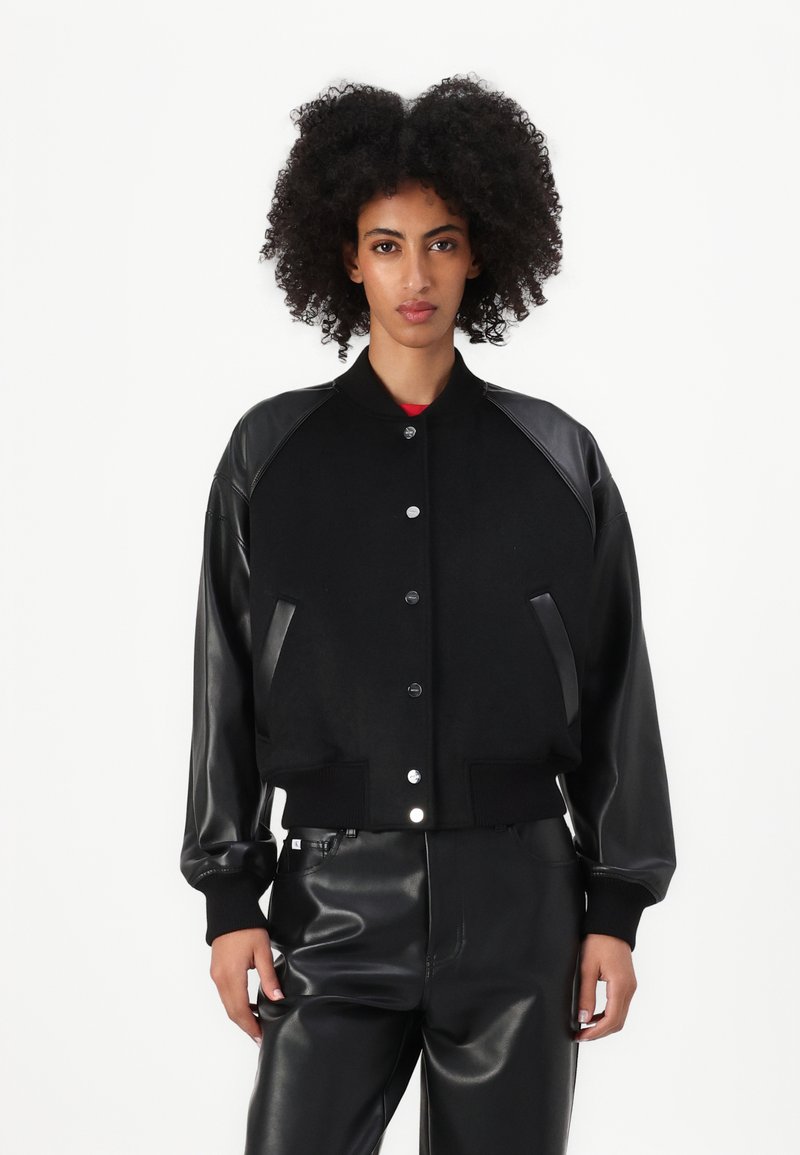 Čierna bunda s koženými rukávmi, rebrovanými manžetami a predným zapínaním na gombíky. Vyrobená z texturovanej látky, s elegantnými líniami a priliehavým strihom.