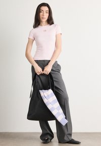 Hele roosa sobiv t-särk lühikeste varrukatega ja väikese logoga, koos hallide triibuliste pükstega ja musta kootud kottiga triibulise sangaga.