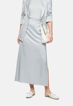 Woman wearing light gray blazer, matching satin midi skirt with side slit, white loafers, and holding a white handbag.