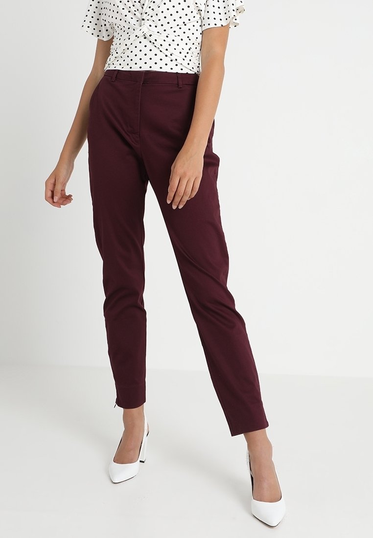 Pantalon bordeaux sur mesure avec une coupe ajustée, doté de poches latérales et d'une texture lisse. Associé à un haut blanc à pois et des talons blancs.