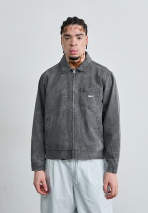 Gray denim jacket with a zip closure, a collar, and a chest pocket featuring "OBEY" logo. Smooth texture with subtle distressed detailing.
