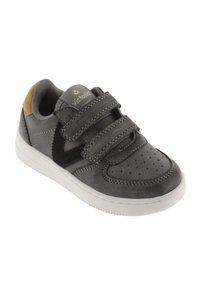 Zapatilla de cuero gris con correas de velcro, puntera perforada, logo negro en contraste y acento de ante beige en el talón. Suela de goma blanca.