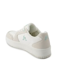 Zapatilla blanca con acentos de ante gris, que cuenta con una suela de goma texturizada y un logo azul claro en el lateral. Diseño de cordones.