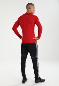 Rode longsleeve sportshirt gecombineerd met zwarte getailleerde broeken met witte strepen. De stof lijkt glad en slim fit, ontworpen voor sportkleding.