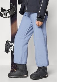 Snowboard pants in light blue, featuring stitching details and elastic cuffs, paired with black snow boots and a snowboard.
