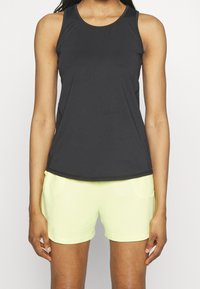 Top sportivo nero con scollatura rotonda, abbinato a pantaloni corti giallo chiaro. Il top presenta una texture liscia e un design aderente.
