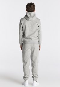 Grau Sweatshirt mit Kapuze und passenden Hosen, aus weichem Stoff, mit gerippten Bündchen und lockerer Passform. Weiße Sneakers runden das Outfit ab.